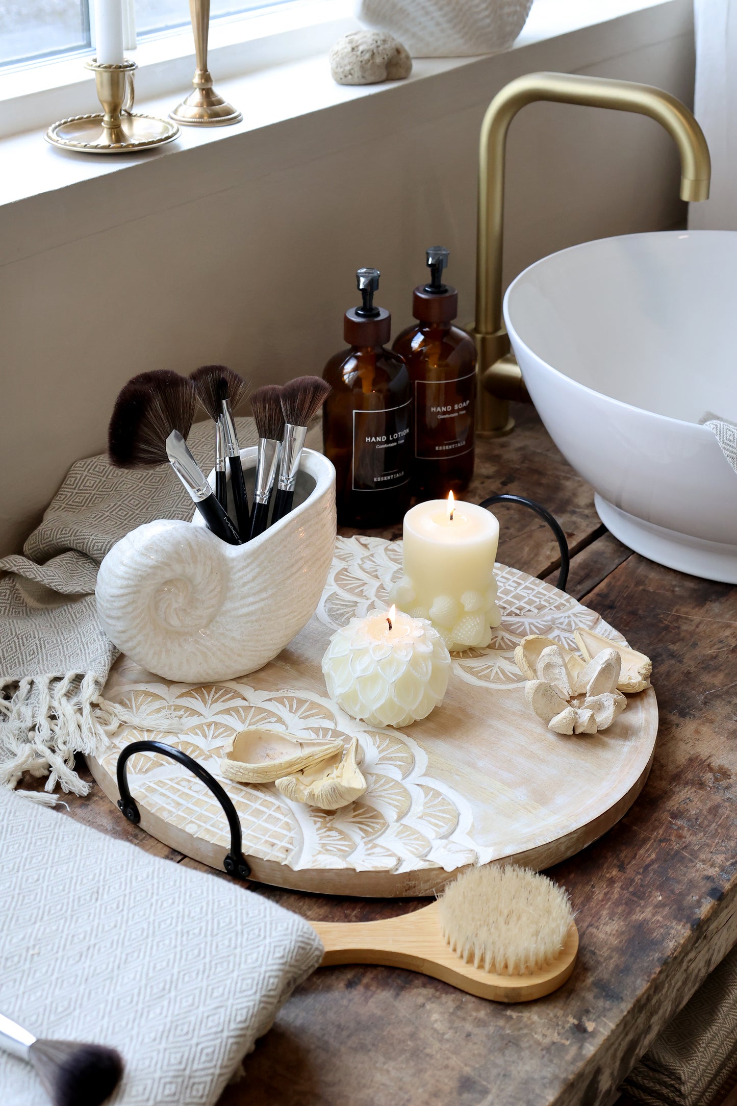 Bathroom counter with skincare products, candles, and a brush on a wooden tray.