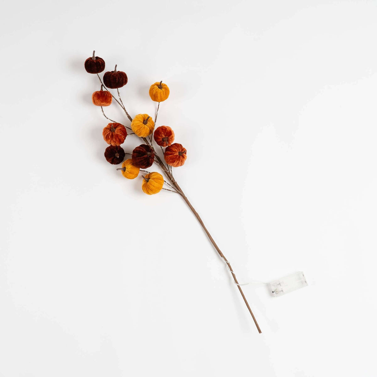 A single decorative faux pumpkin branch with multiple small velvet pumpkins in orange, dark orange, and burgundy on a brown stem, photographed on a clean white background with a small clear tag attached.