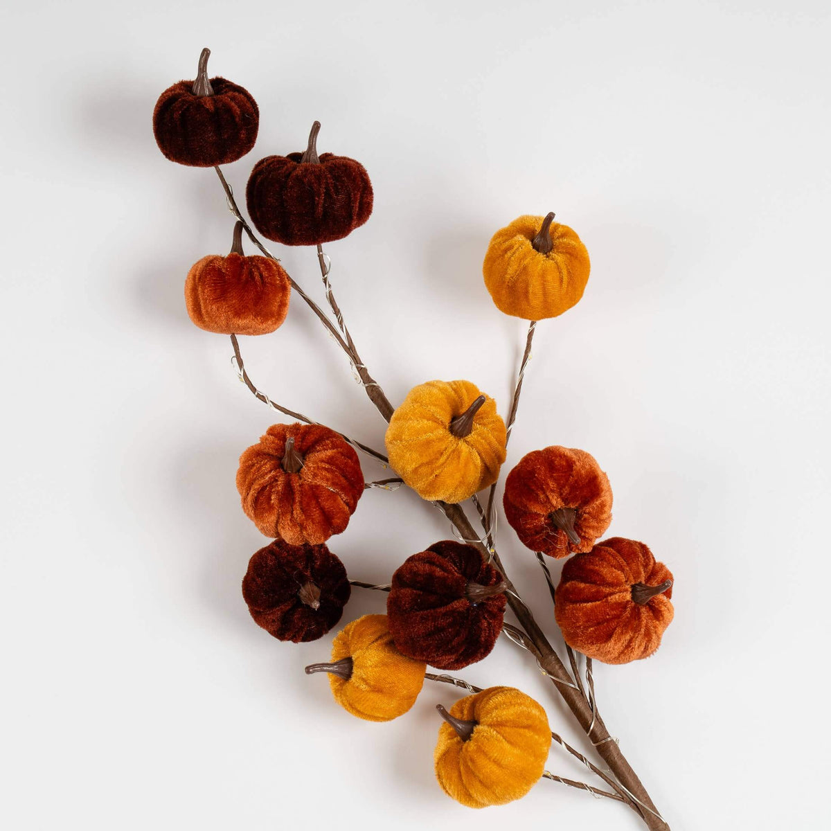 Autumn velvet pumpkin branch with small fabric pumpkins in orange, rust, and dark brown on brown stems, photographed on a clean white background.
