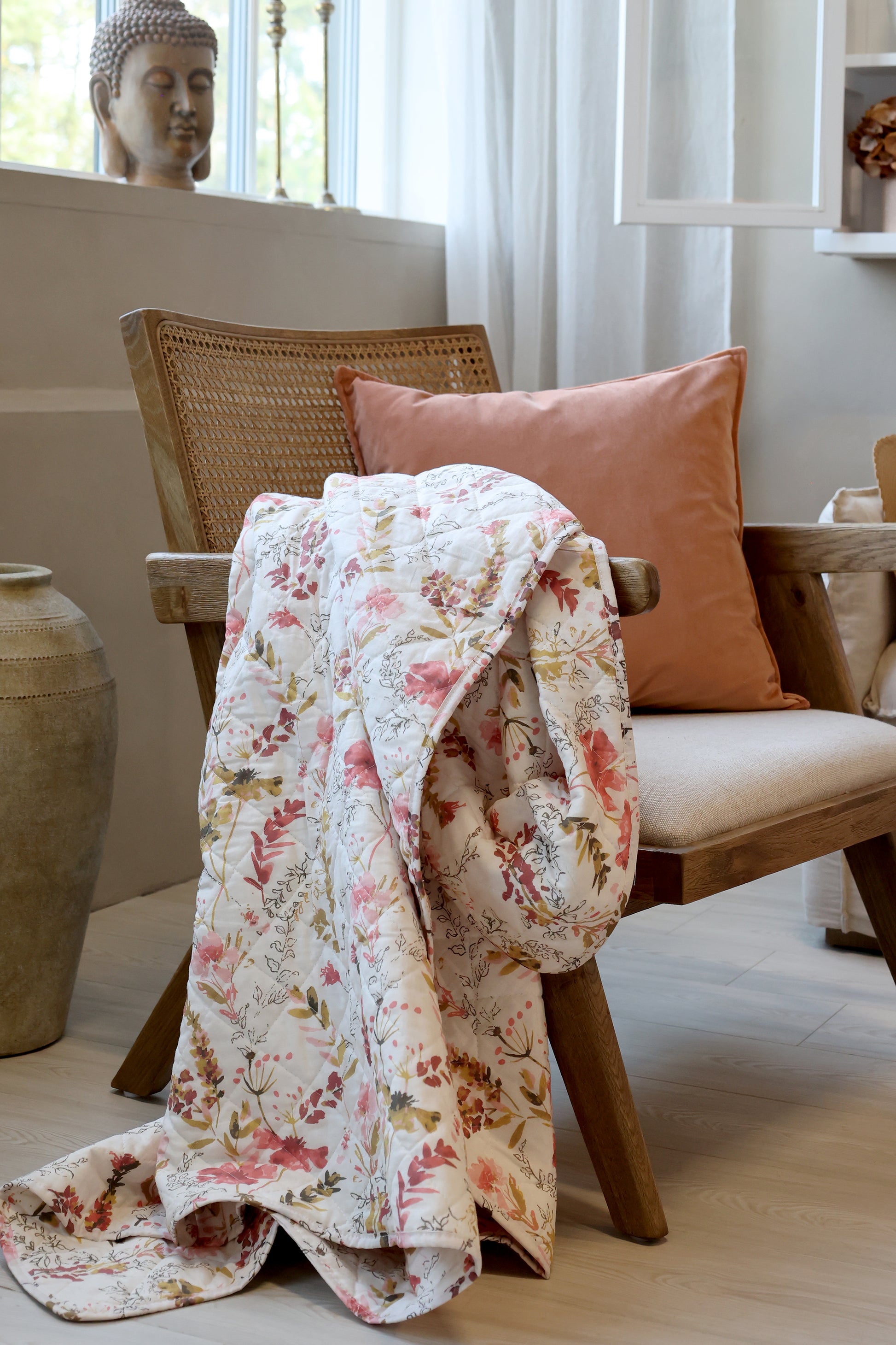 Floral quilt draped over a chair with a pink pillow in a room setting.