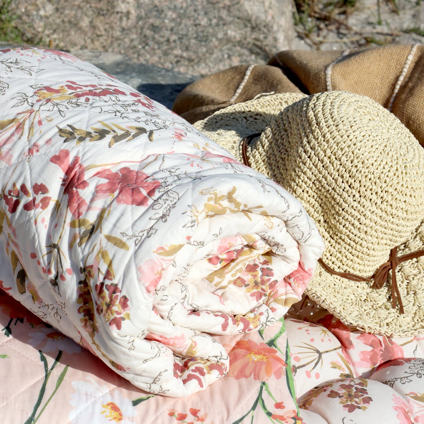 Floral-patterned blanket and straw hat on a stone surface