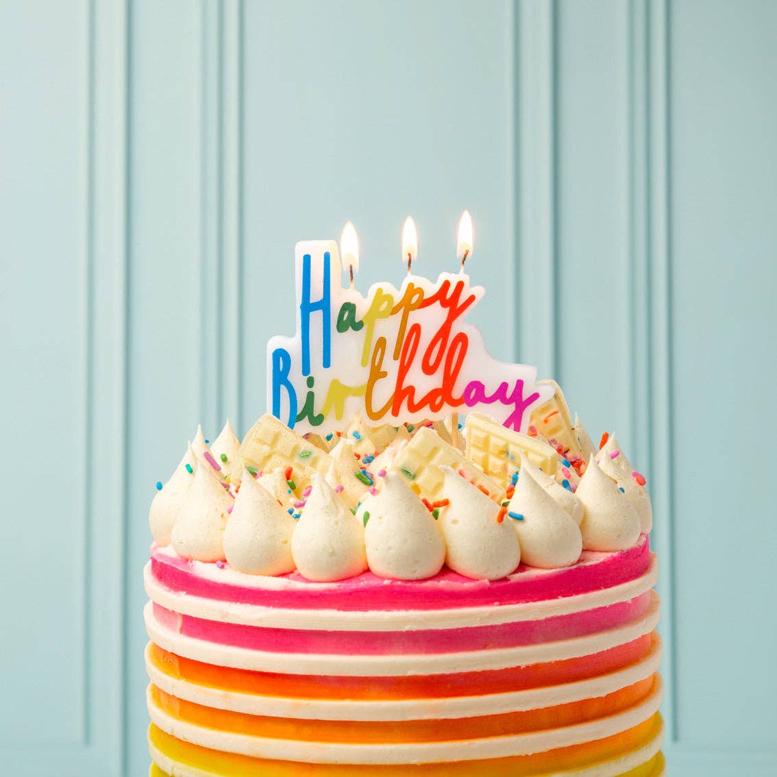 Colorful birthday cake with 'Happy Birthday' candles on a light blue background