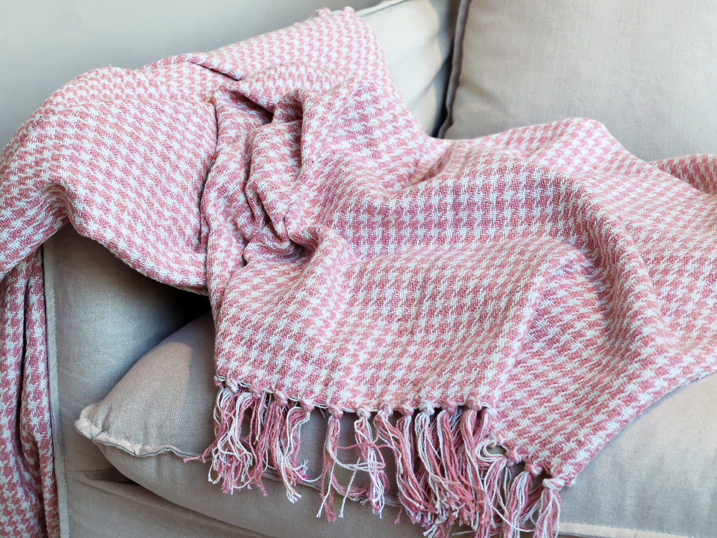 Pink woven blanket with fringes draped over a light-colored sofa.