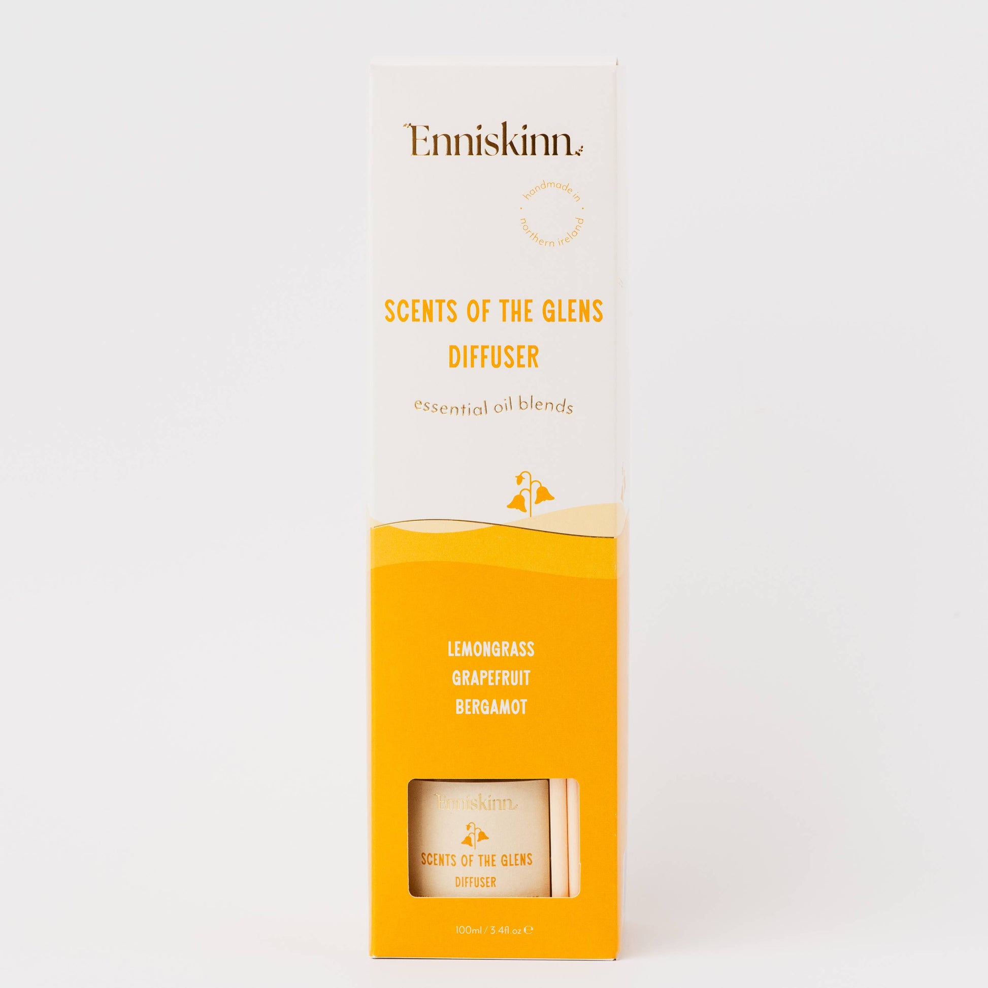 A tall rectangular product box for Enniskinn Scents of the Glens Diffuser, shown upright on a clean white background. The packaging is primarily white on the upper half and bright yellow-orange on the lower half, with black and yellow text and a small clear window near the bottom revealing part of the diffuser inside.