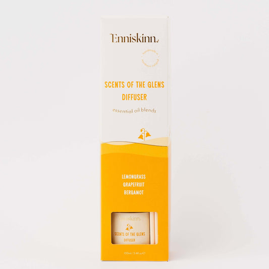 A tall rectangular product box for Enniskinn Scents of the Glens Diffuser, shown upright on a clean white background. The packaging is primarily white on the upper half and bright yellow-orange on the lower half, with black and yellow text and a small clear window near the bottom revealing part of the diffuser inside.