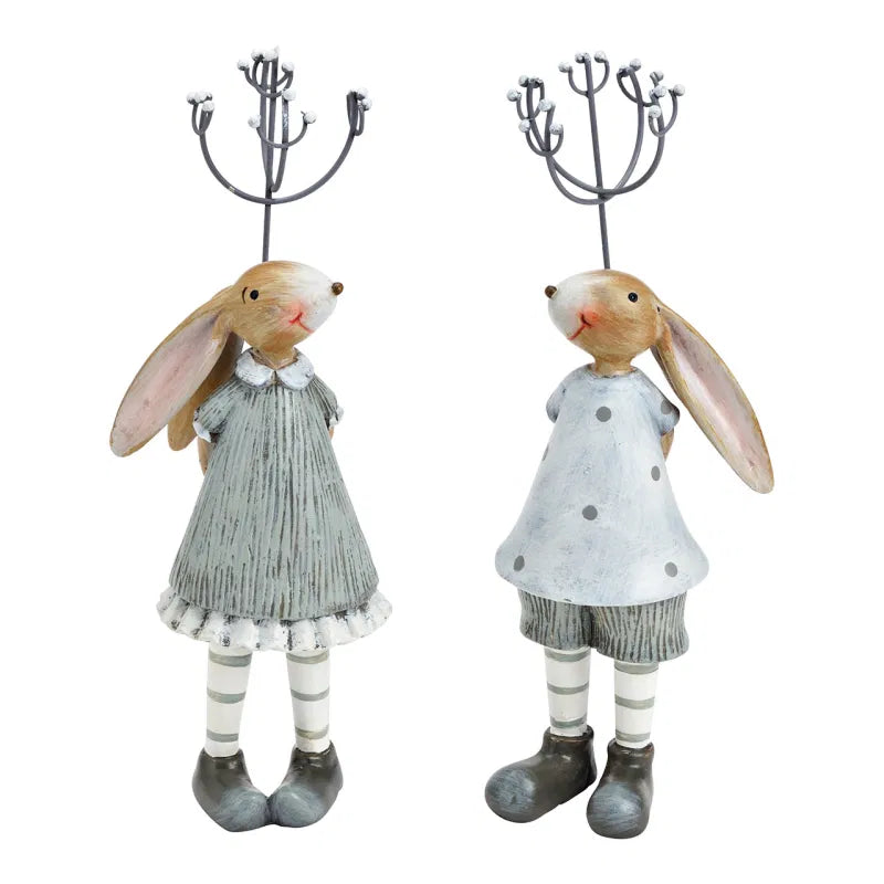 Two decorative rabbit figures in dresses with candle holders on a white background
