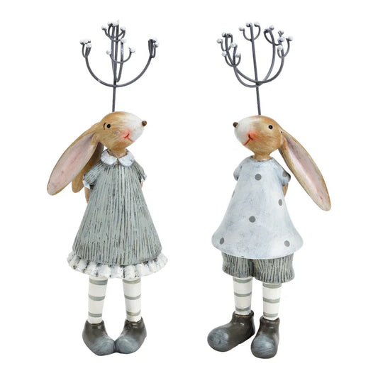 Two decorative rabbit figures in dresses with candle holders on a white background