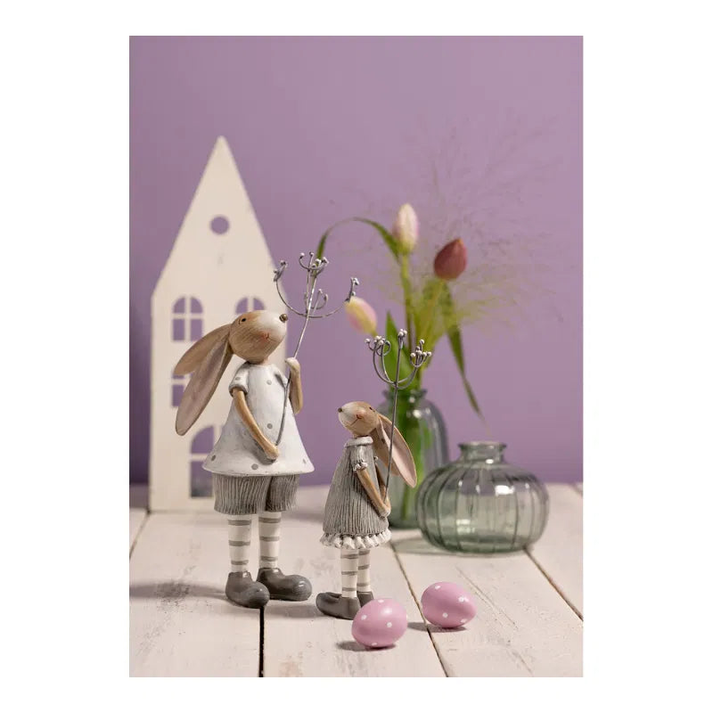 Two decorative rabbit figures with a vase of flowers and eggs on a wooden surface against a purple wall.