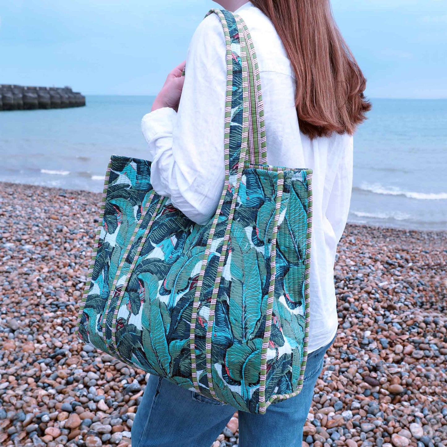 Person holding a green patterned bag on a pebbly beach with ocean in the background