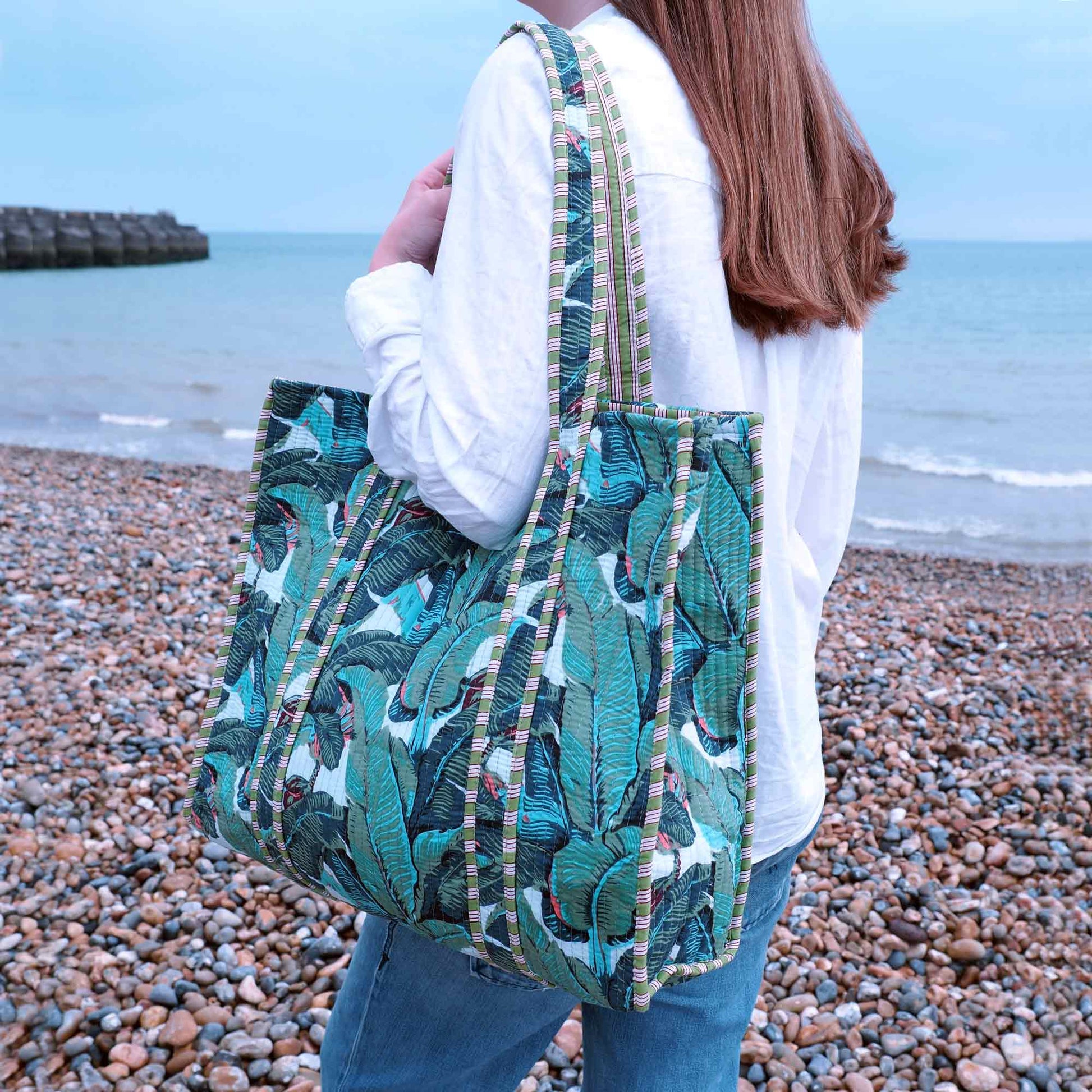 Person holding a green patterned bag on a pebbly beach with ocean in the background