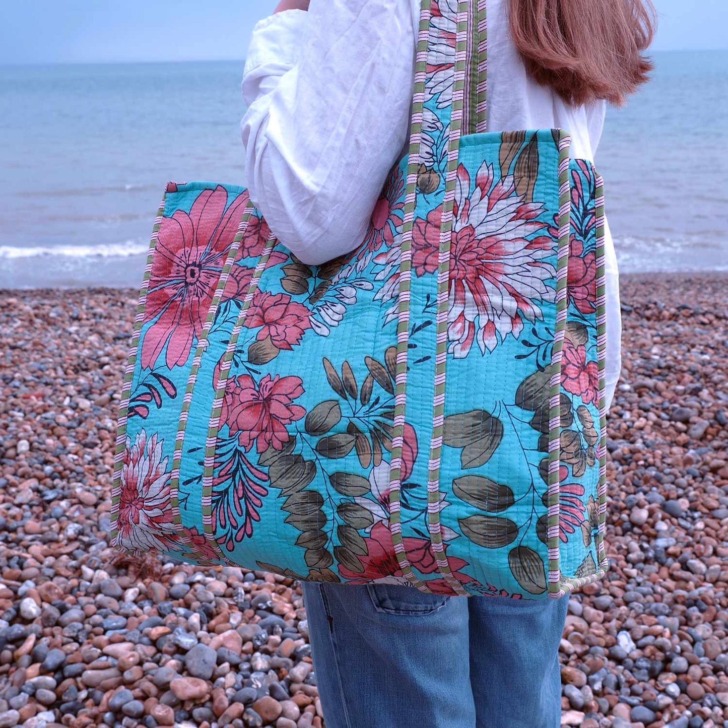 Person holding a floral tote bag on a pebbly beach