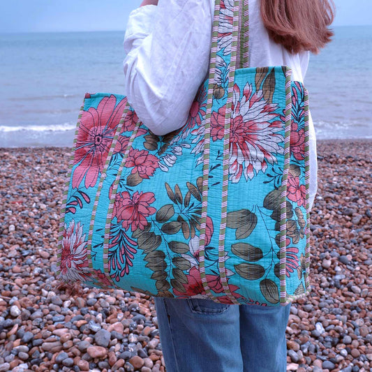 Person holding a floral tote bag on a pebbly beach