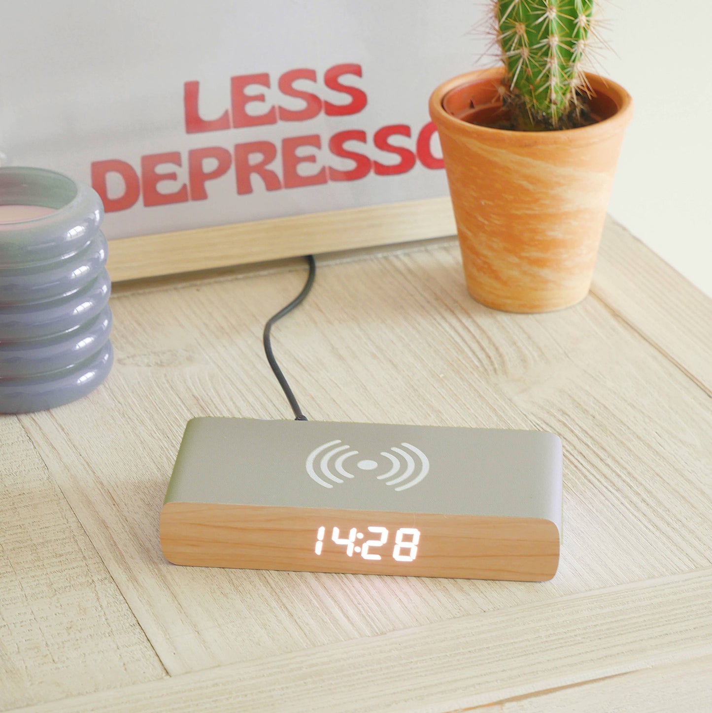 Digital clock with wooden bottom on a wooden surface, next to a potted cactus and motivational poster.