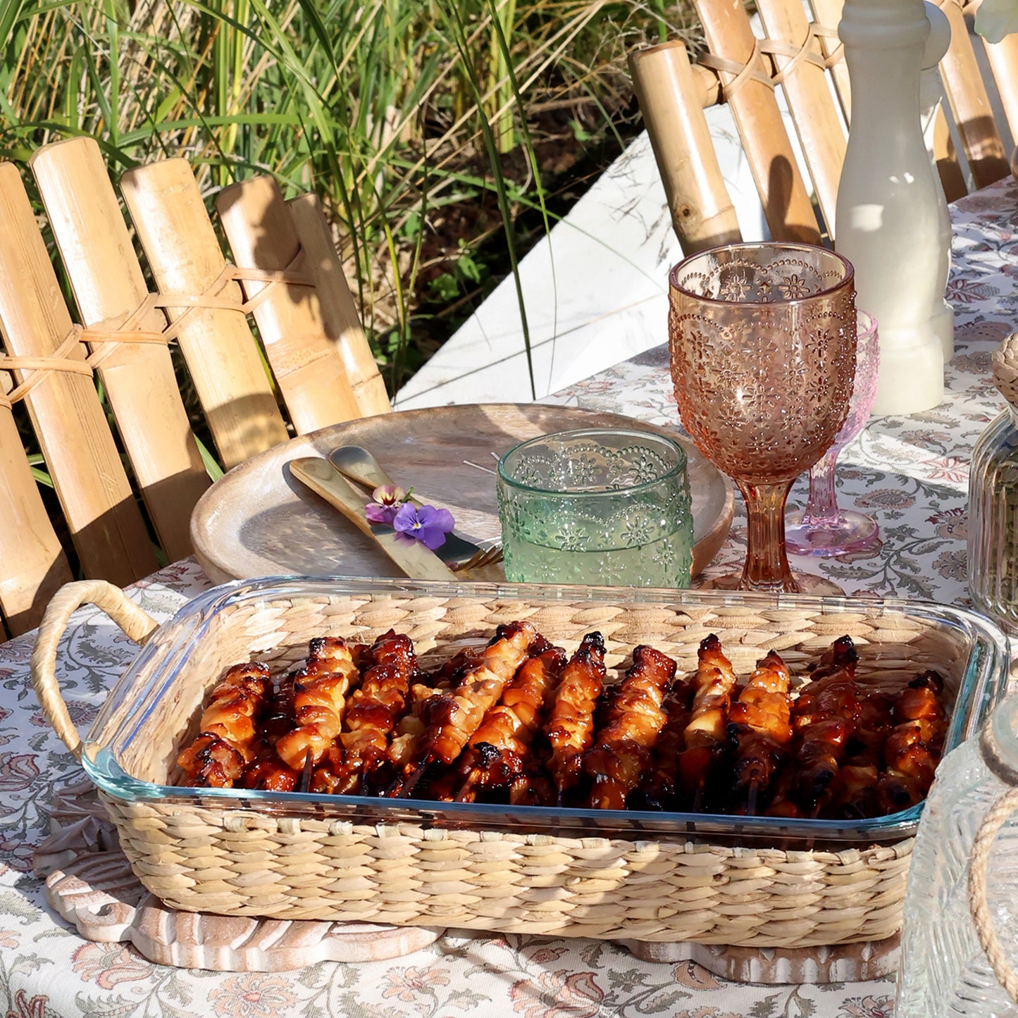 Basket of grilled skewers on a table with glasses and cutlery outdoors