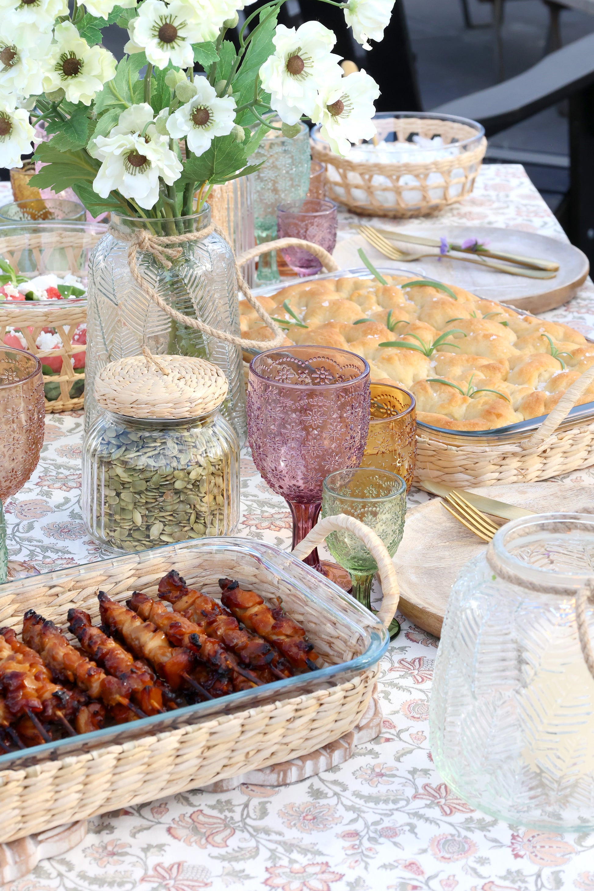 Outdoor dining table with food, drinks, and flowers on a floral tablecloth
