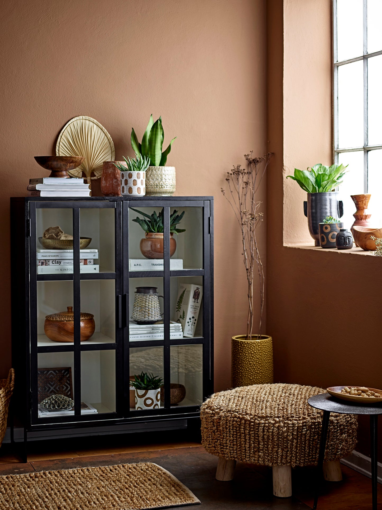 Room interior with a dark glass cabinet, plants, and a woven stool.