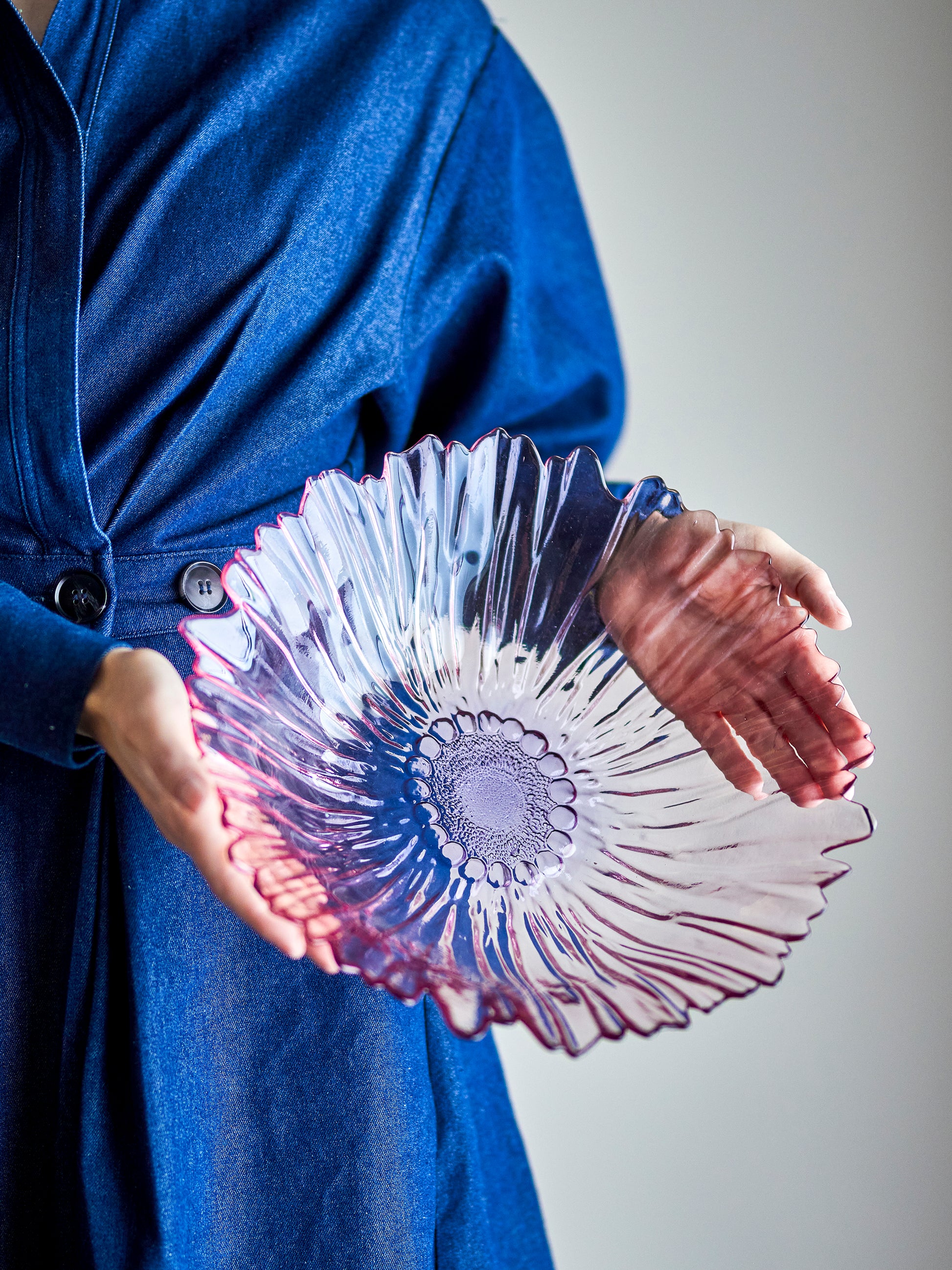 Person holding a decorative glass bowl with a blue coat