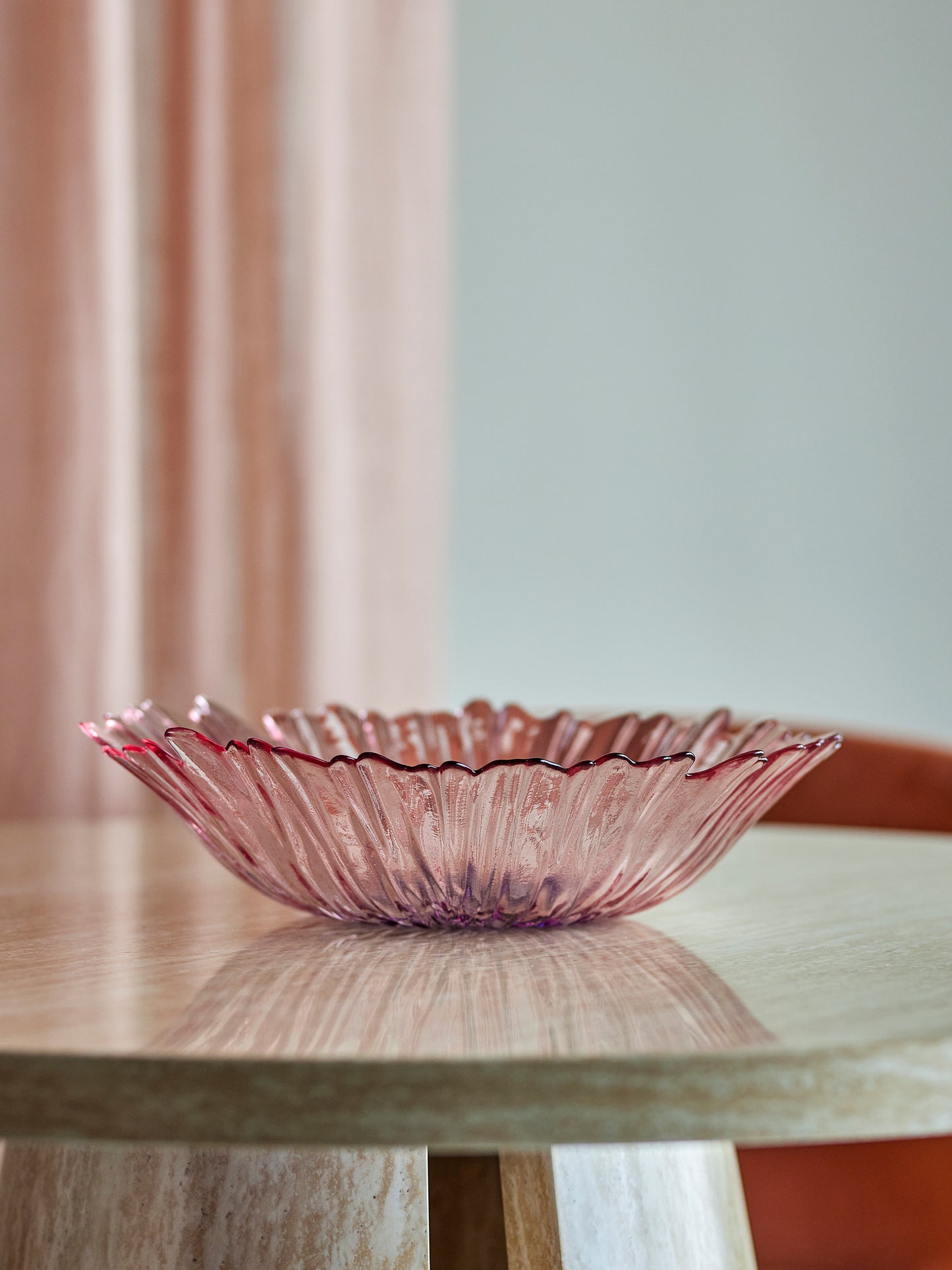 Pink glass bowl on a wooden table with a blurred curtain in the background