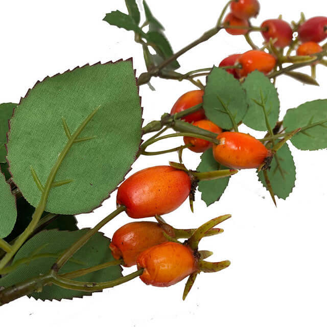 Artificial rosehip branch with green textured leaves and clusters of orange-red berries on a white background.