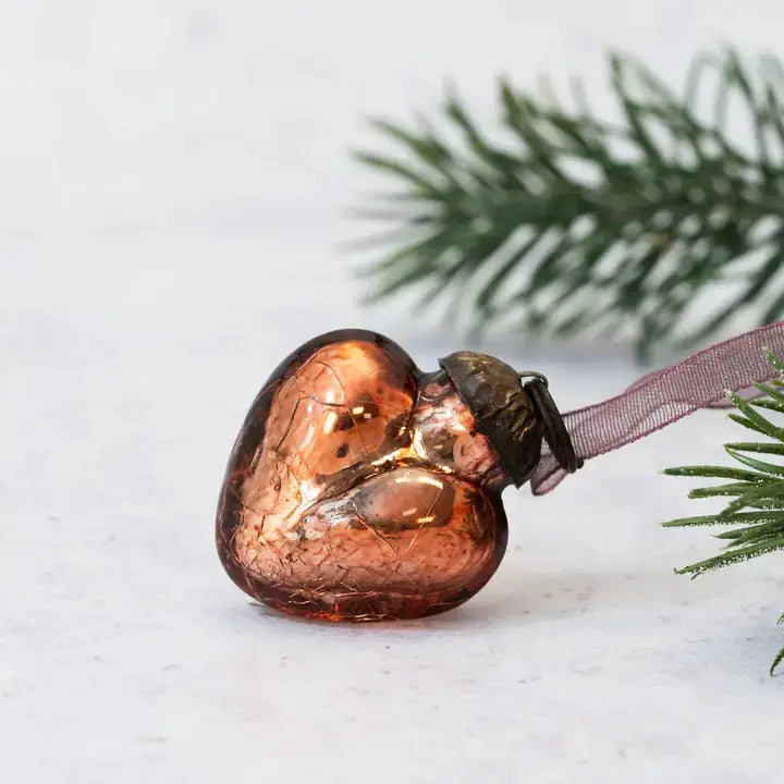 Heart-shaped glass ornament on a branch with snow