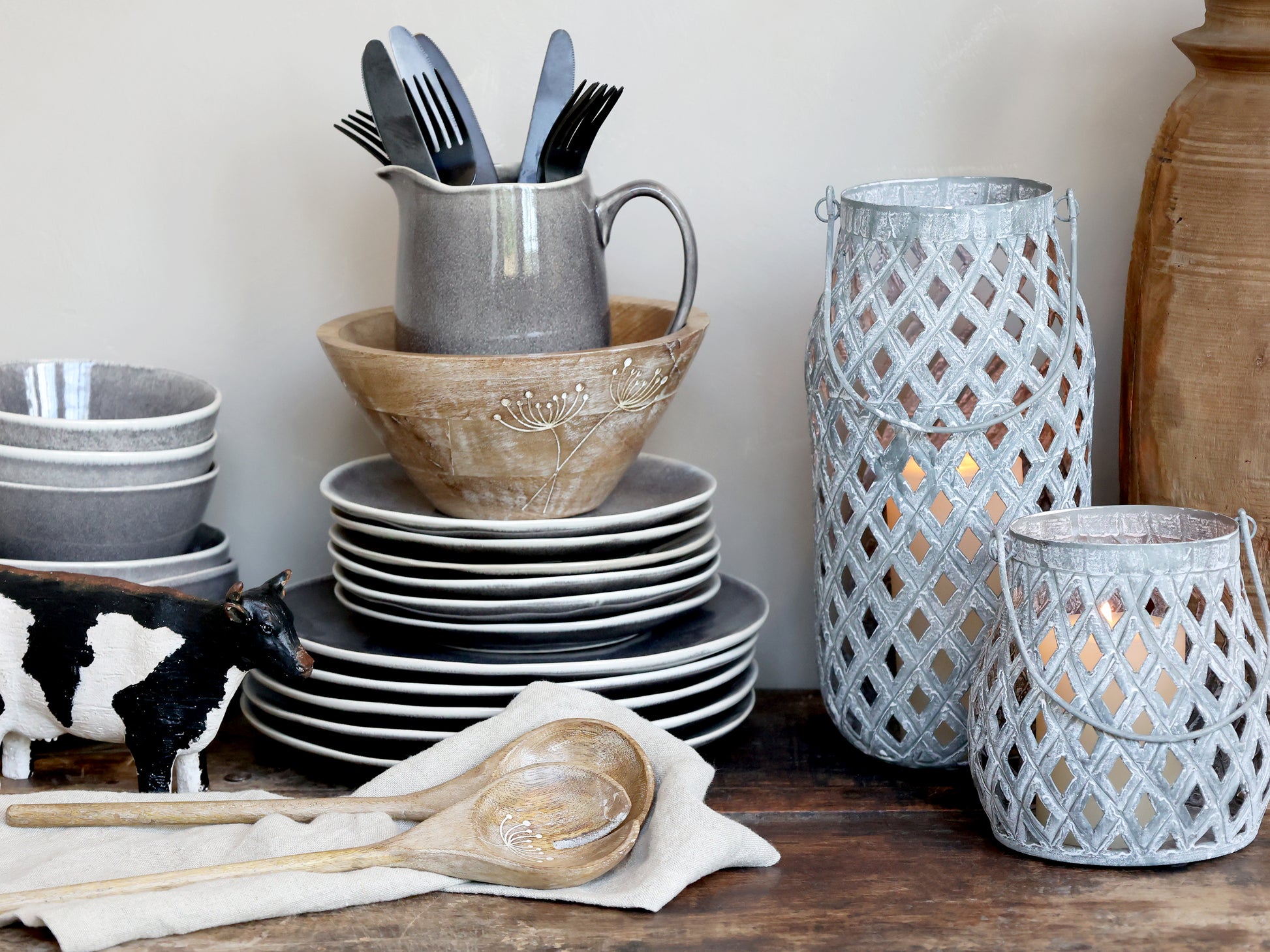 Dishes, including plates, bowls, and a pitcher, on a wooden surface with decorative lanterns and a cow figurine.
