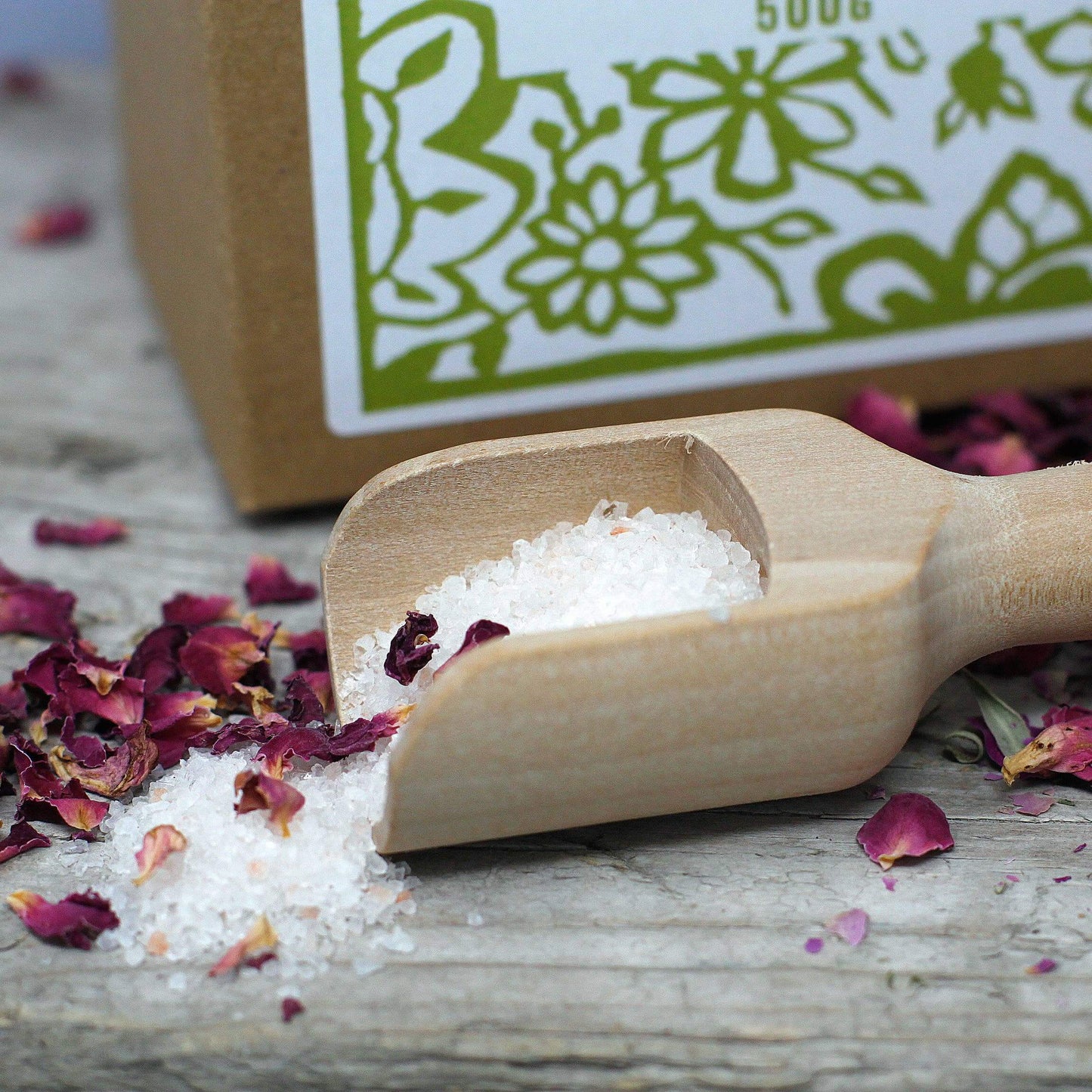 Agnes + Cat Lavender Himalayan bath salts in a wooden scoop with dried rose petals.