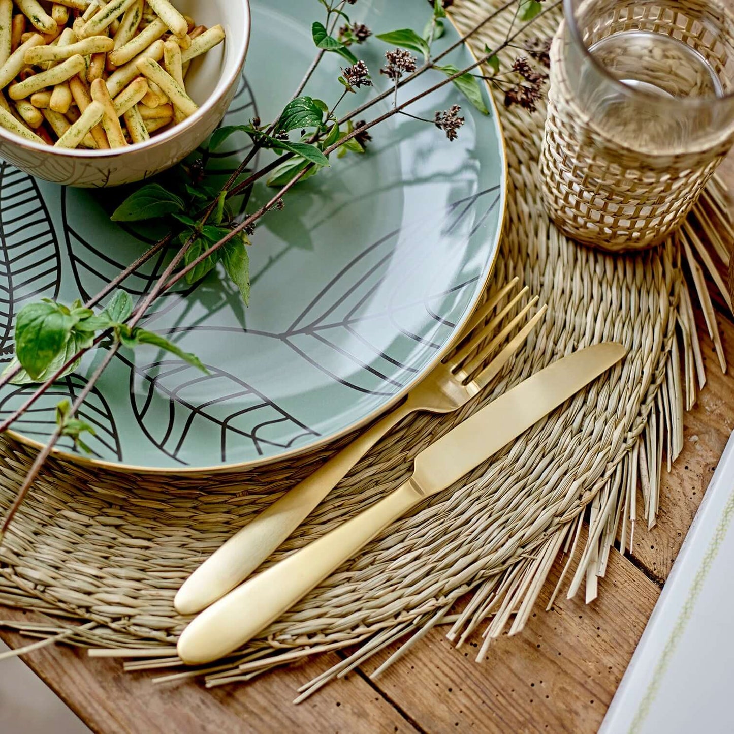 Table setting with a plate, bowl of snacks, and cutlery on a woven placemat.