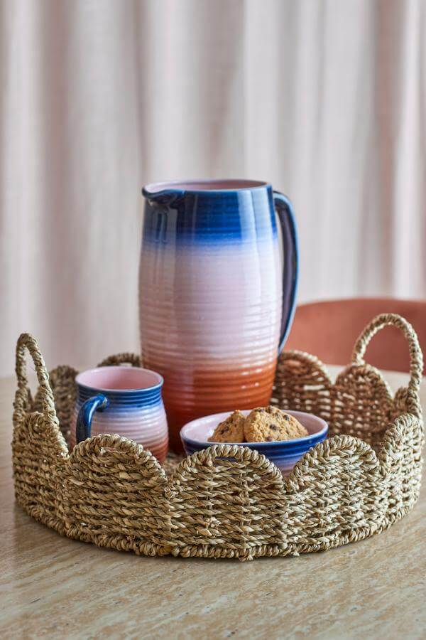 Woven basket with ceramic pitcher and mugs on a neutral background