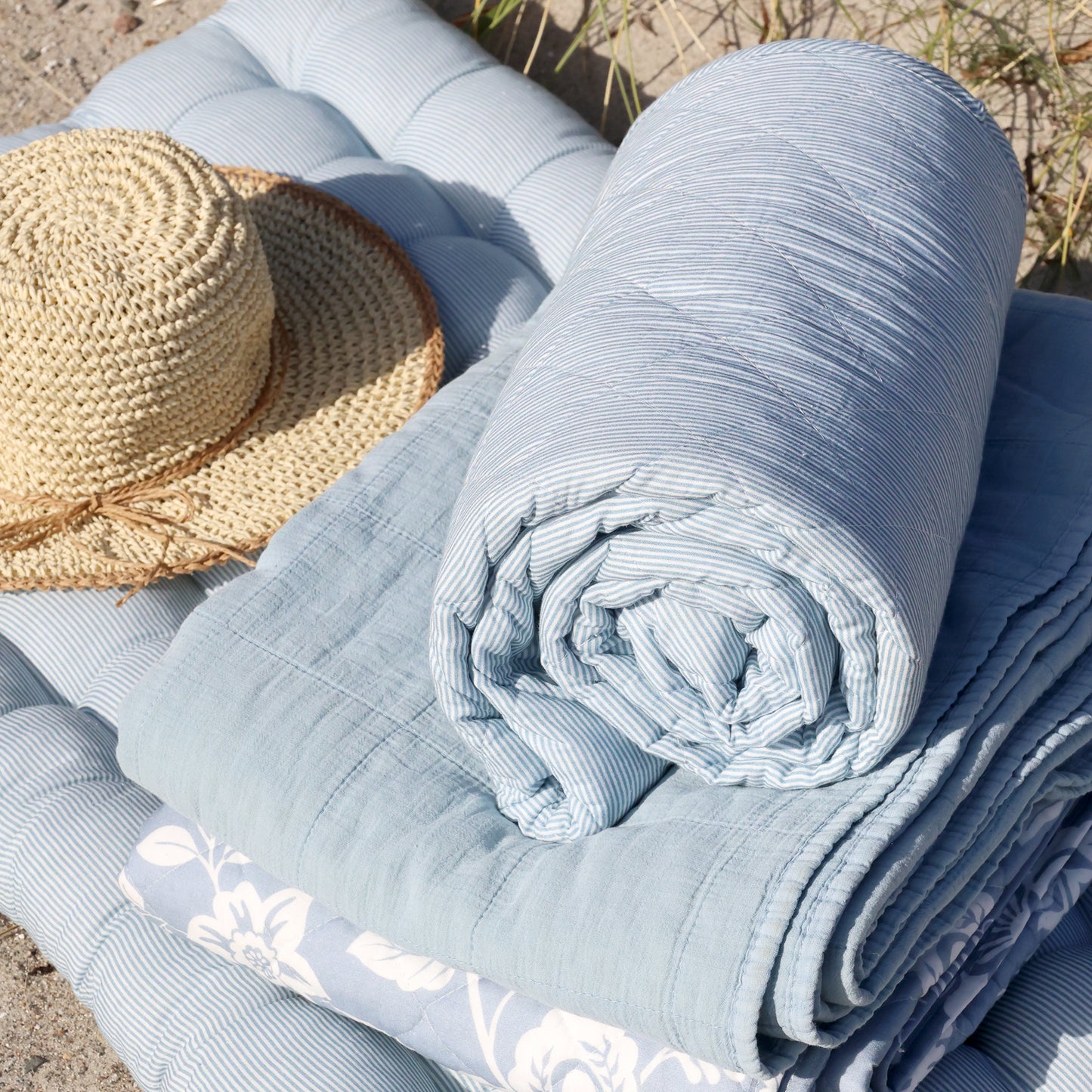 Rolled-up light blue fabric on a textured surface with a straw hat nearby