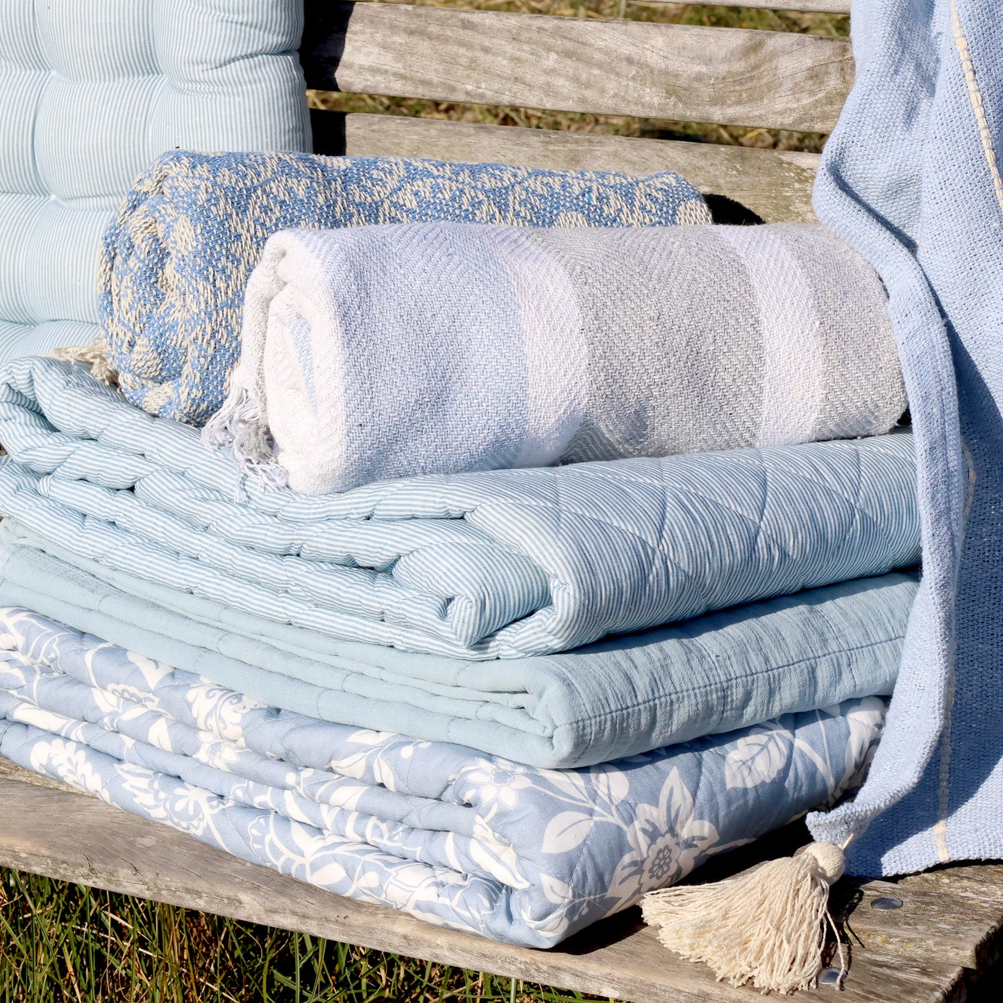 Stack of folded towels and blankets on a wooden bench outdoors