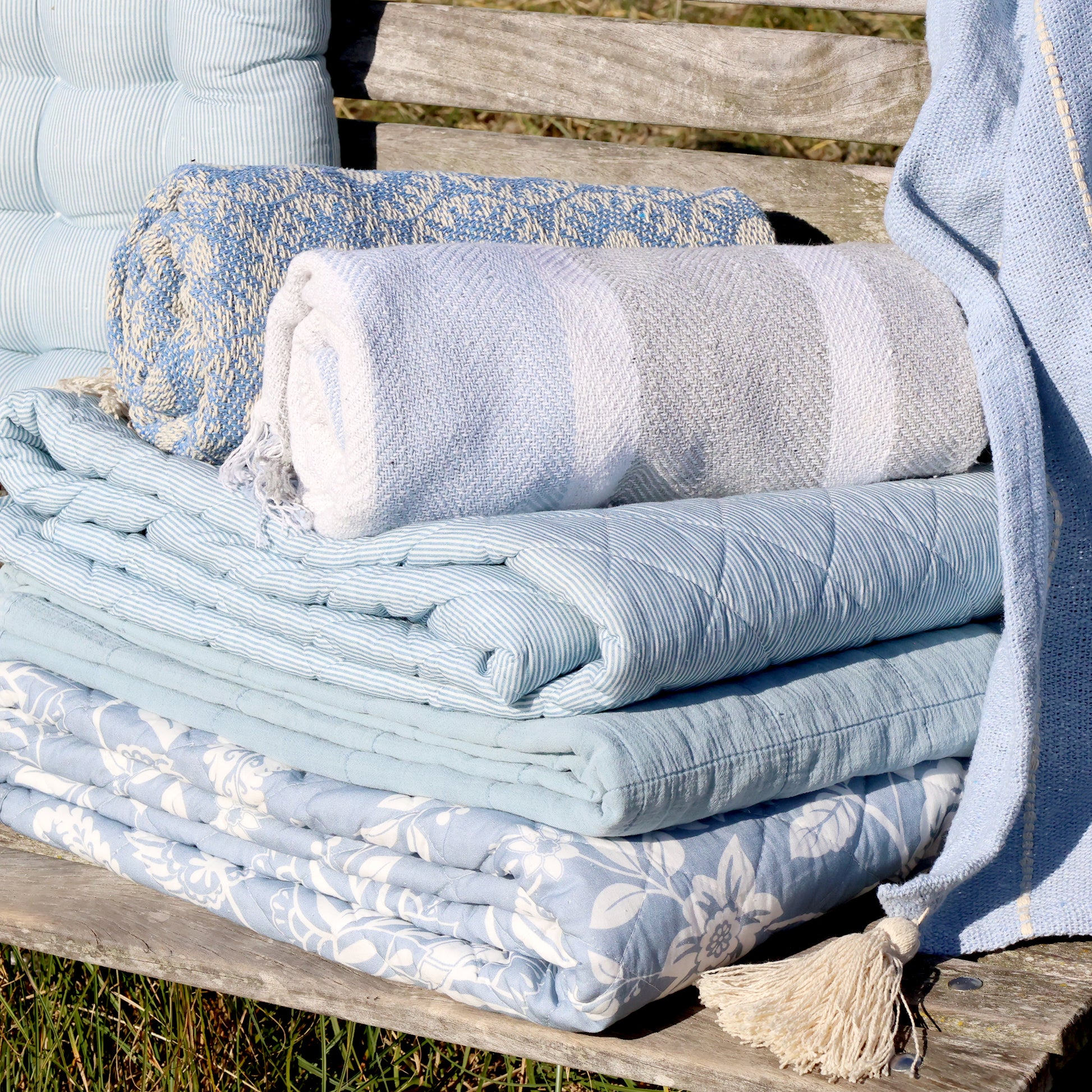 Stack of folded towels and blankets on a wooden bench outdoors
