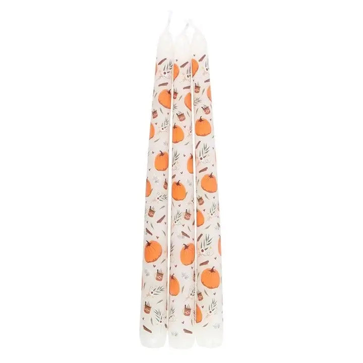 Three taper candles standing upright, featuring an orange and brown pumpkin pattern on a white background.