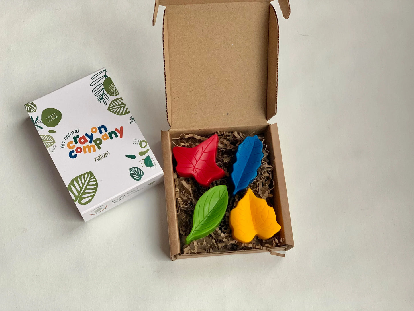 Colorful leaf-shaped crayons in a box with a branded box on a light background.