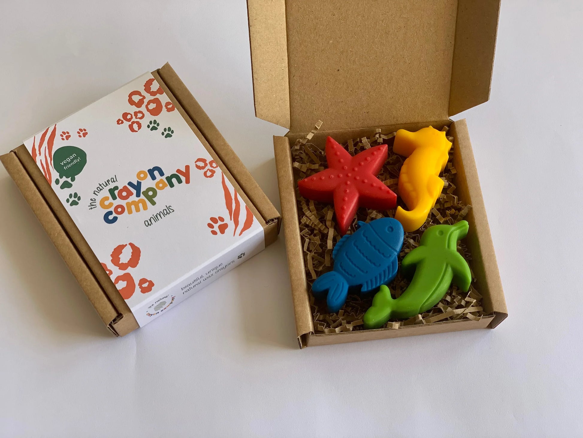 Colorful animal-shaped crayons in a box with a branded card on a white background