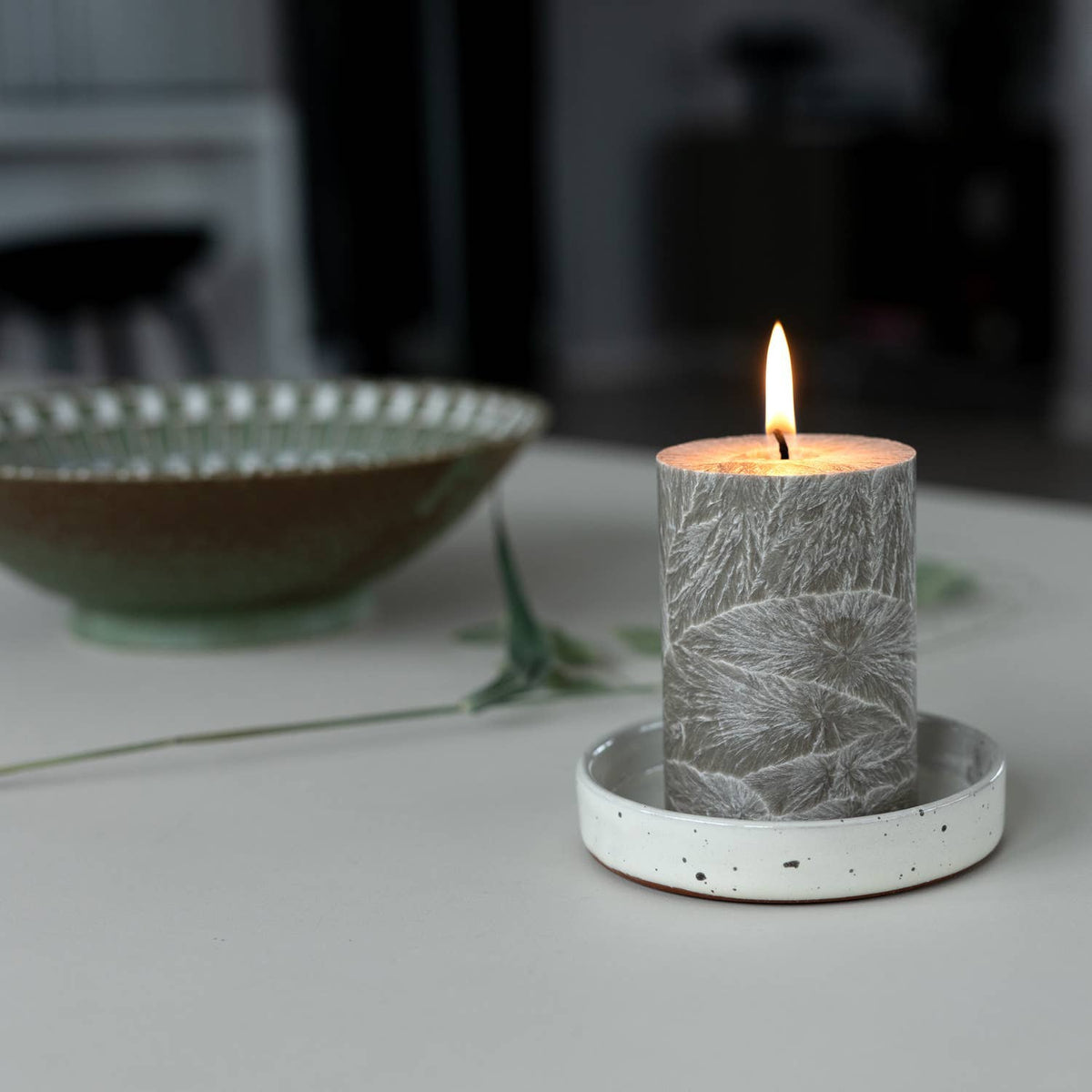 Gray textured candle in a white holder on a blurred background