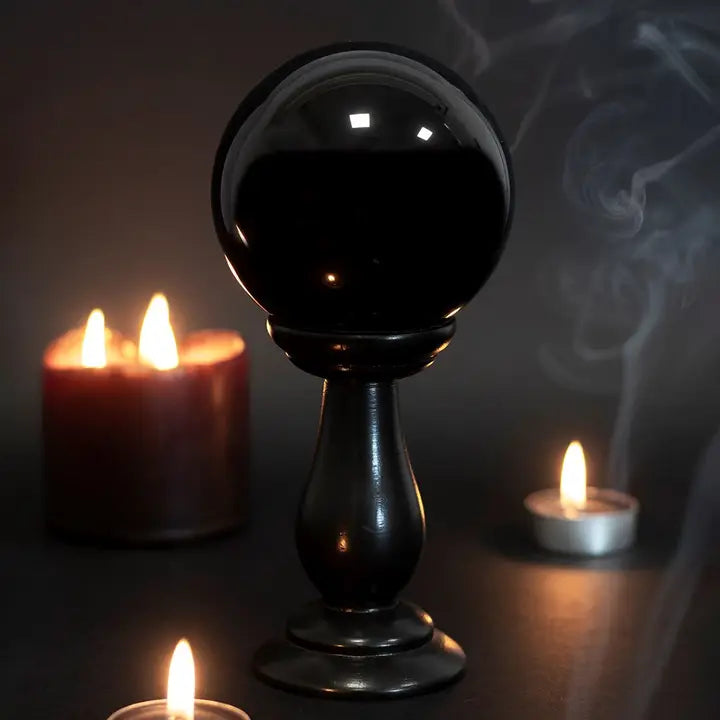 Black crystal ball on a stand with candles in the background