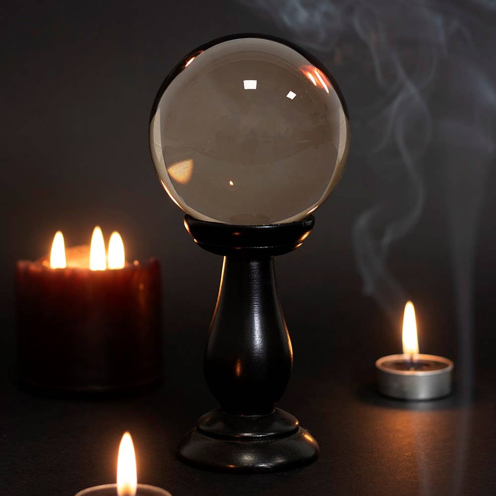 Vintage-style smoke grey crystal ball on a stand with candles in the background
