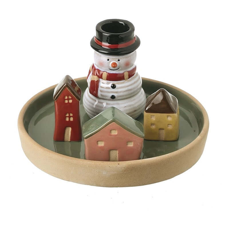 Ceramic snowman candle holder with a hat and scarf, surrounded by small houses on a round dish.