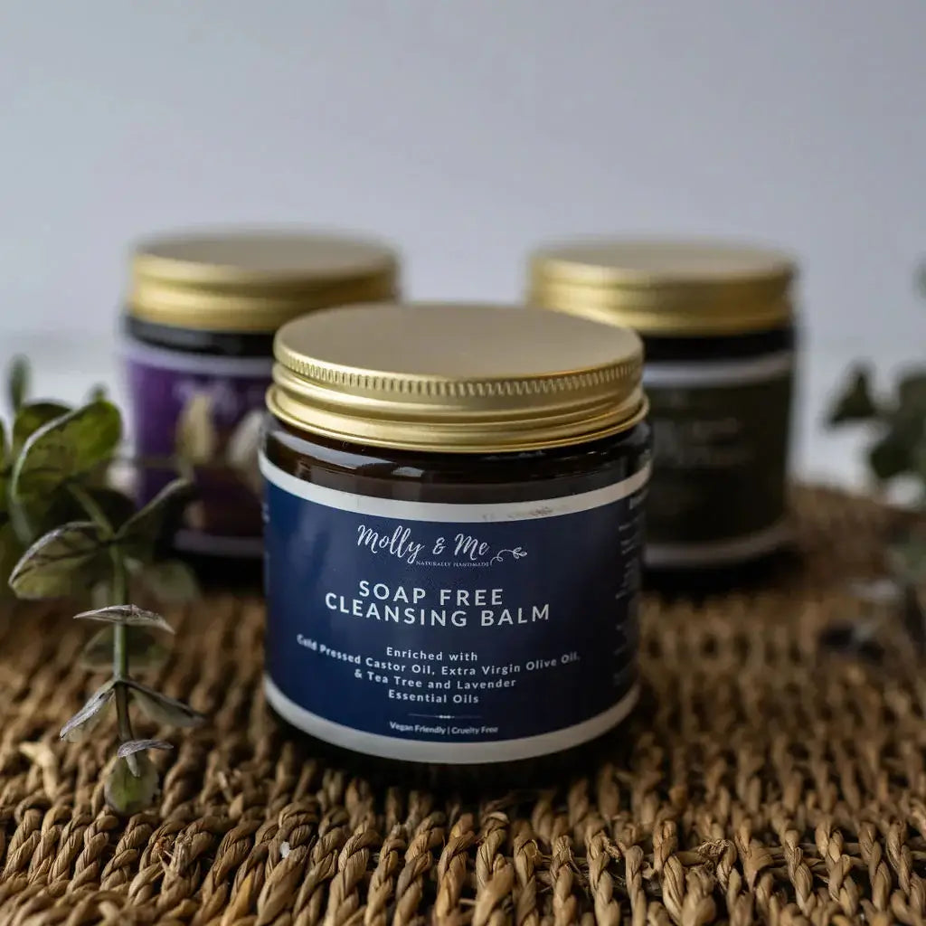 Soap-free cleansing balm jar with gold lid on a woven surface, surrounded by plants.