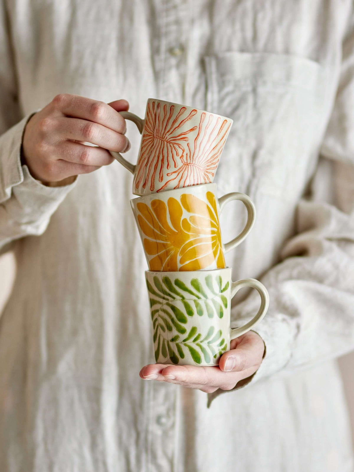 Stack of three ceramic mugs with leaf patterns held by a person wearing a light-colored shirt.