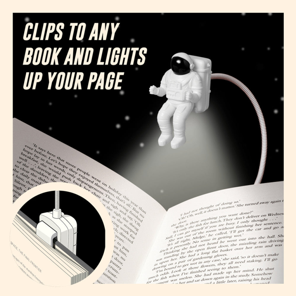 Astronaut-shaped book light clips to an open book, illuminating a page.