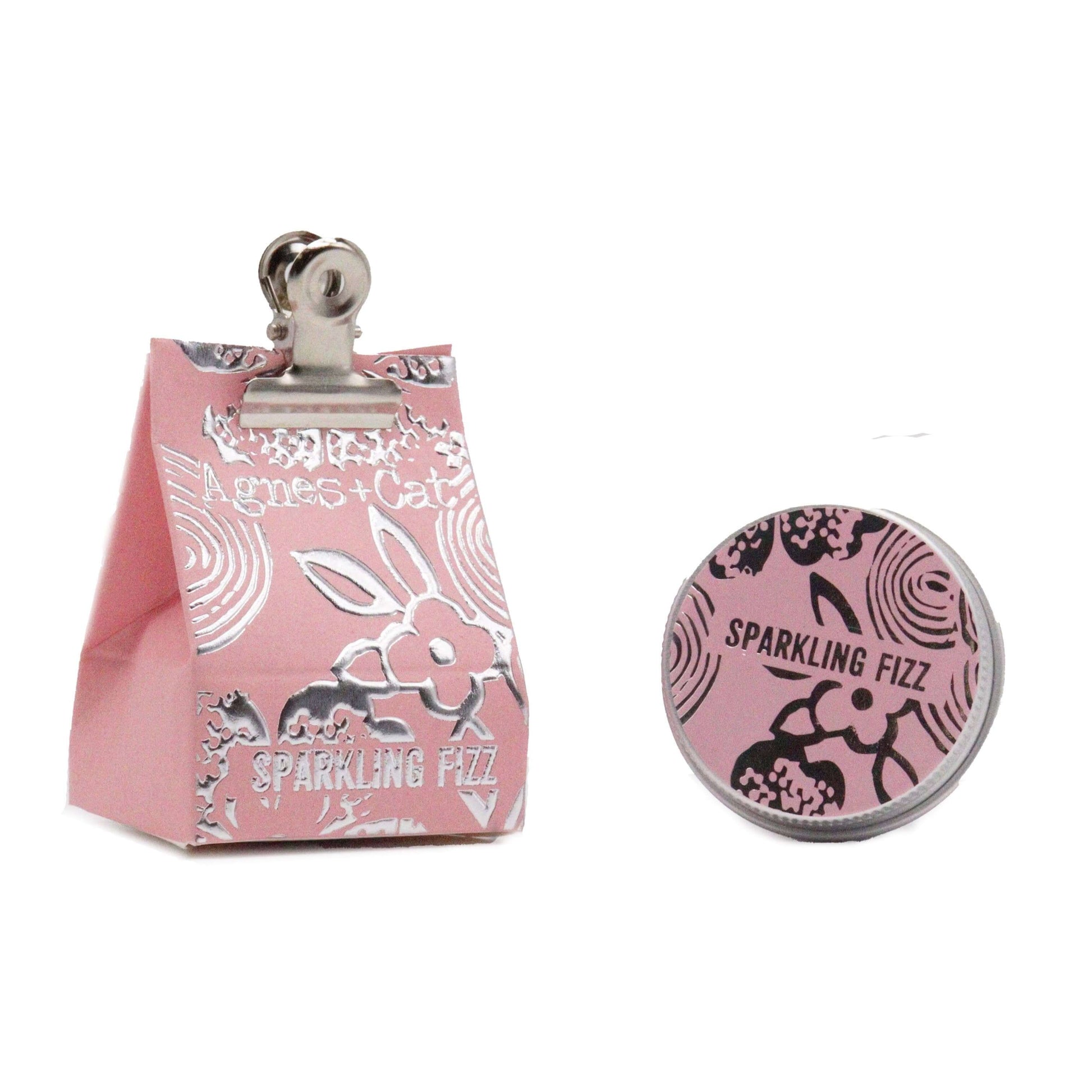 A pink lip balm packaging with 'Agnes & Cat Sparkling Fizz' printed on it, featuring floral patterns, next to a tin of lip balm