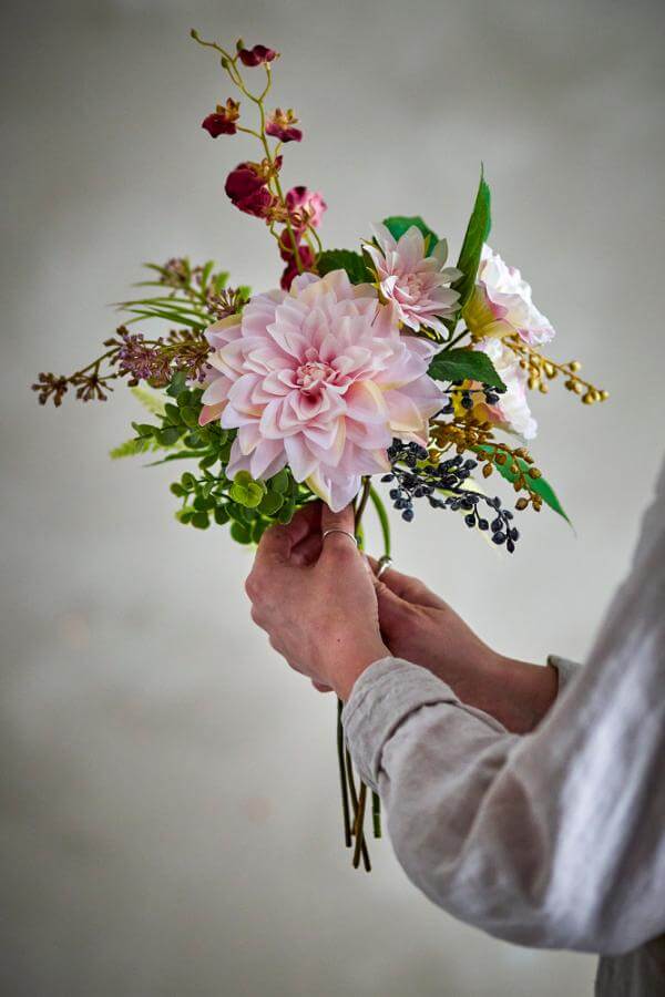 Person holding a bouquet of pink flowers against a neutral background
