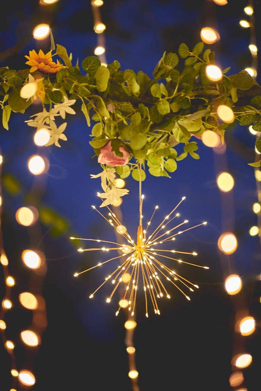 Decorative string lights with flowers and a sparkler against a dark blue sky.