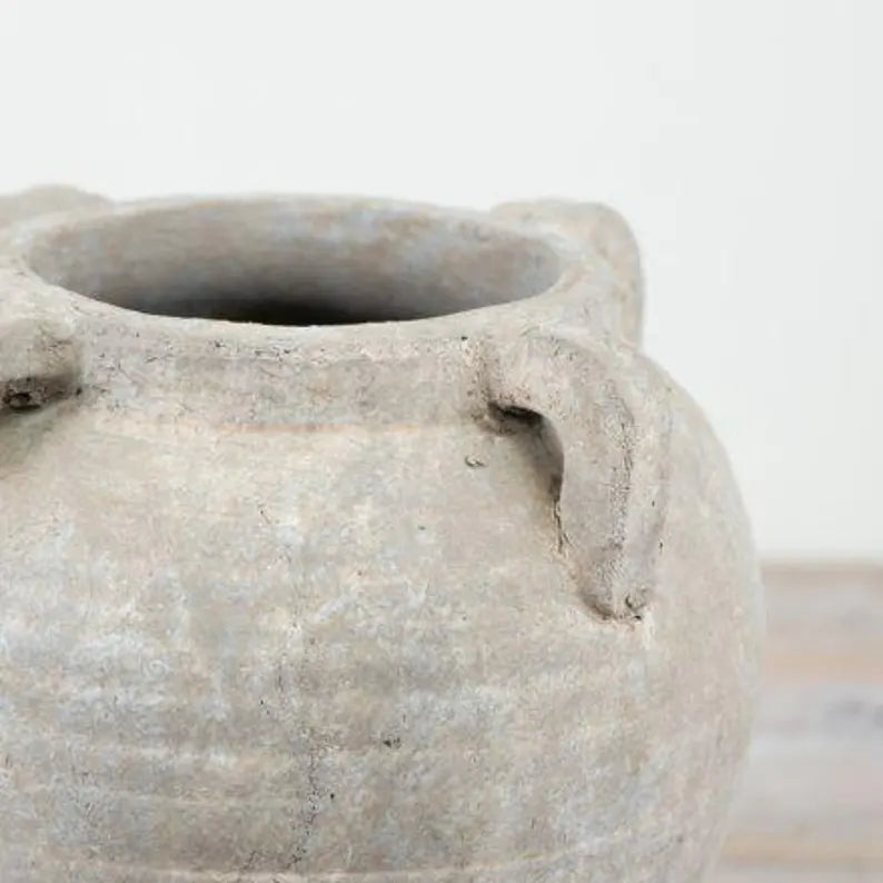 Close-up of a textured stone pot with handles on a light background