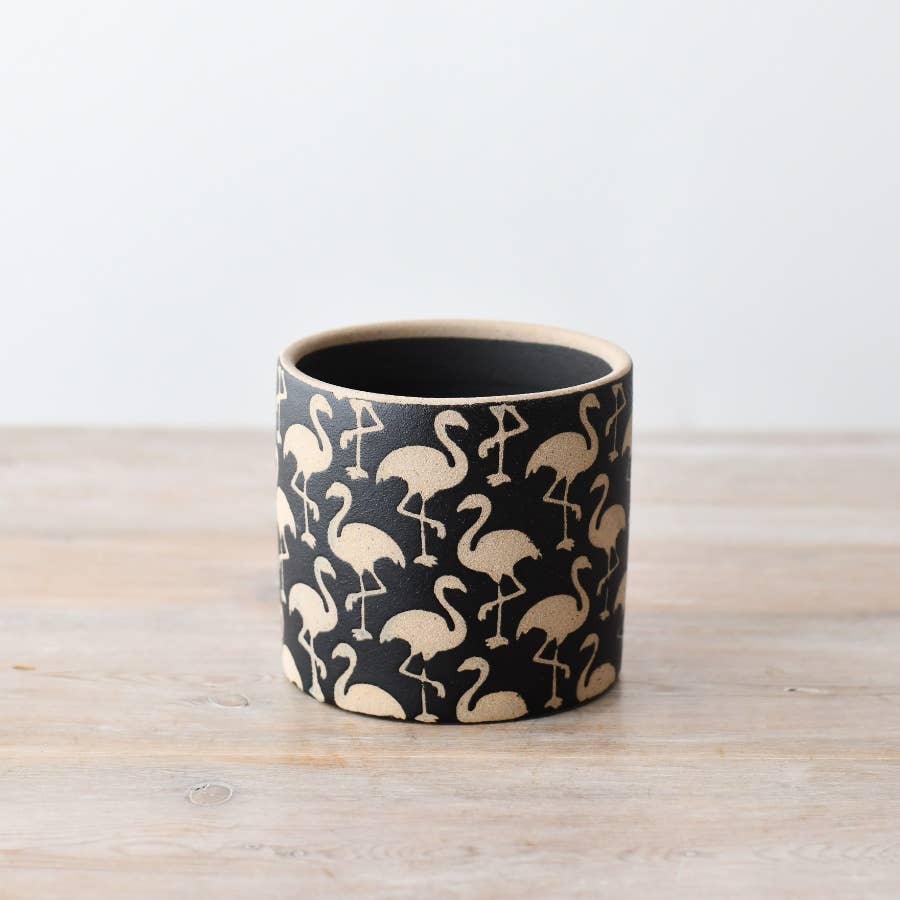 A cylindrical stoneware planter with black and cream flamingo pattern detailing, placed on a wooden surface.