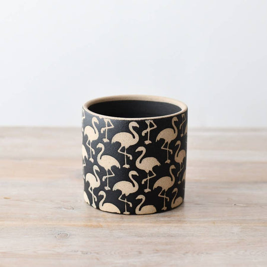 A cylindrical stoneware planter with black and cream flamingo pattern detailing, placed on a wooden surface.