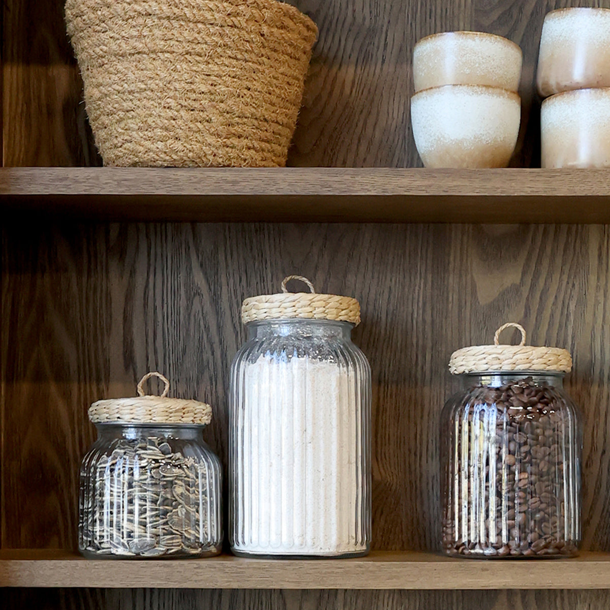 Ribbed glass storage jar with wicker lid on shelves