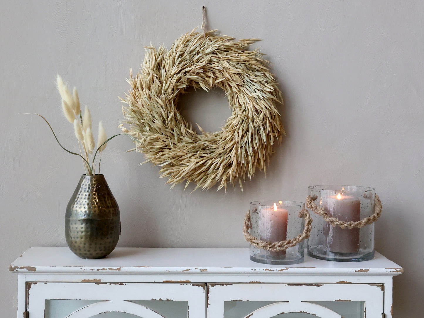Decorative wreath above a white cabinet with candles and a vase.