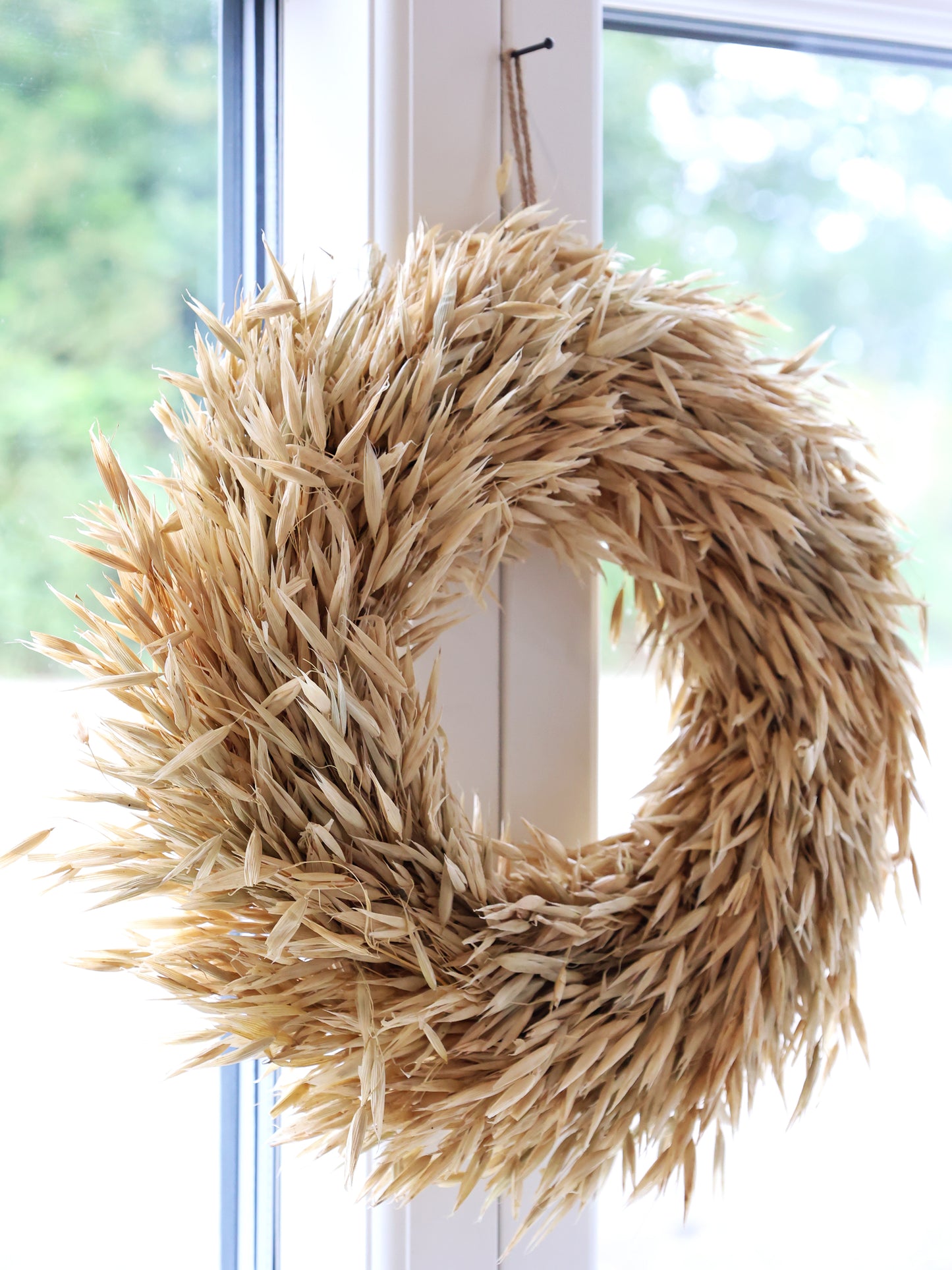 Wheat wreath hanging on a white door with a blurred green and blue background